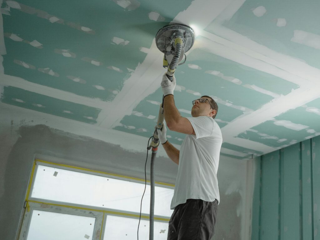 man on wall sanding drywall